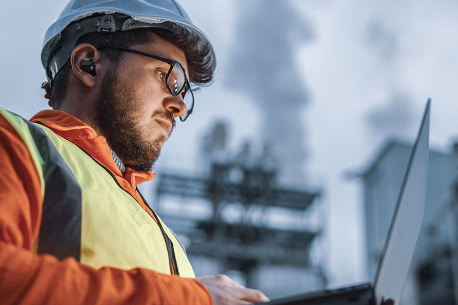 A Civil Construction worker from Superior Skilled Trades operating a laptop in front of a factory.